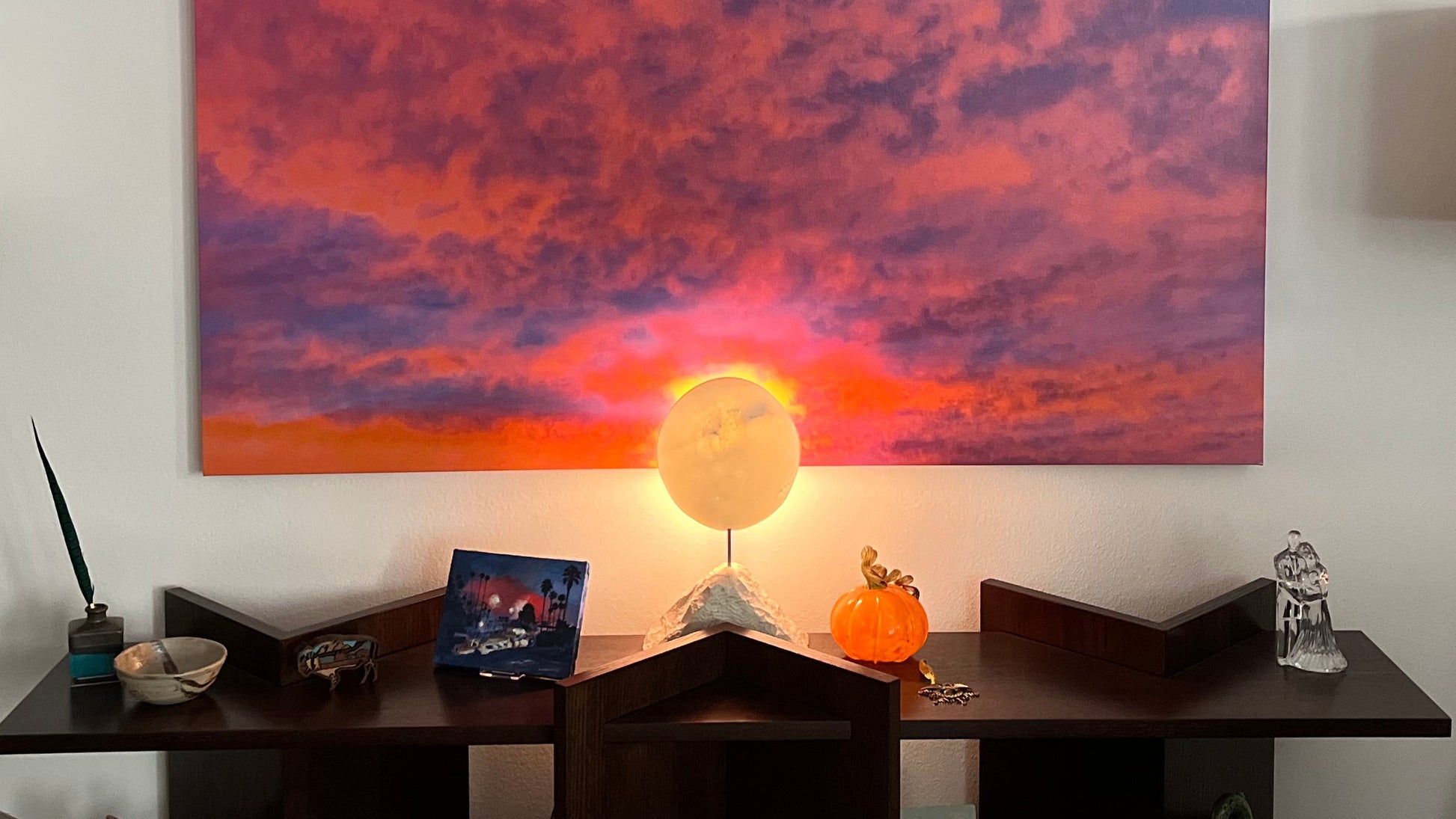 Living room with a colorful sunset phot on the wall, two lamps, and a small table and back lighting on the Moon Phases sculpture. 
